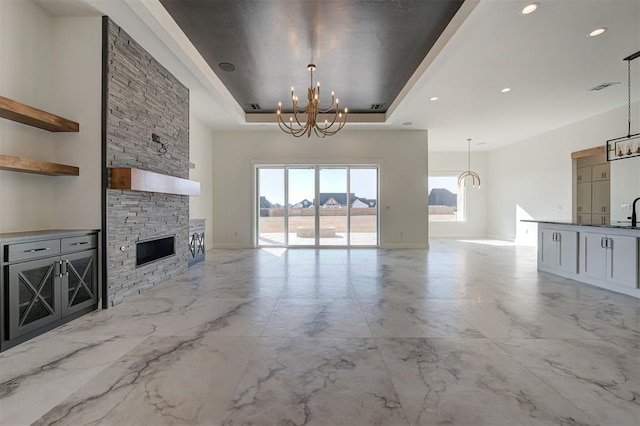 unfurnished living room featuring a fireplace, a chandelier, and a raised ceiling