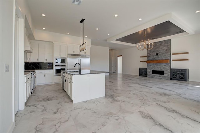 kitchen with white cabinetry, a tray ceiling, built in appliances, and an island with sink