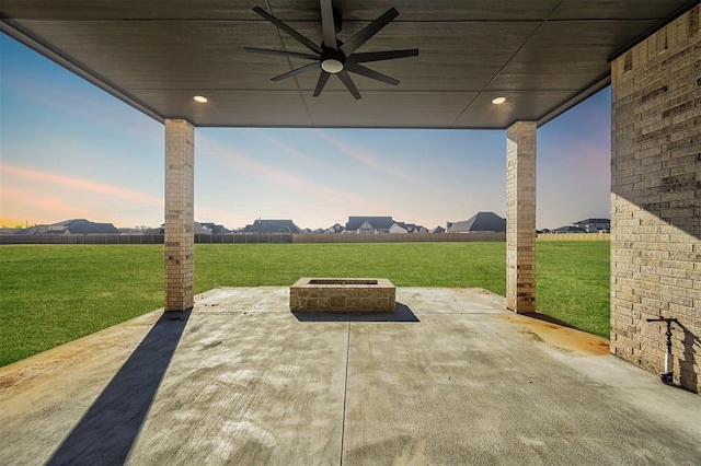 patio terrace at dusk with ceiling fan, a yard, and a fire pit