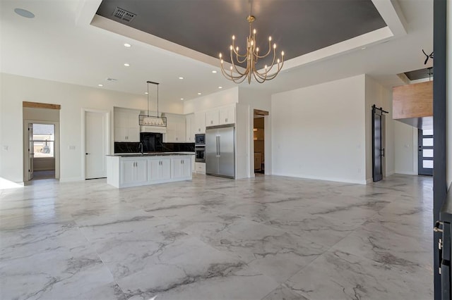 interior space with decorative light fixtures, a center island, a raised ceiling, a barn door, and white cabinets