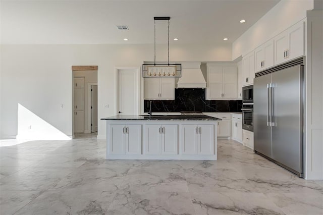 kitchen featuring custom exhaust hood, white cabinetry, pendant lighting, and built in appliances