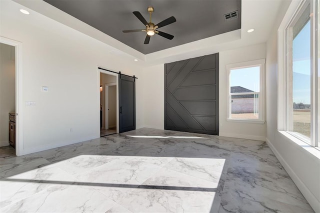 empty room with ceiling fan, a tray ceiling, and a barn door