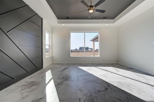 empty room with ceiling fan and a tray ceiling