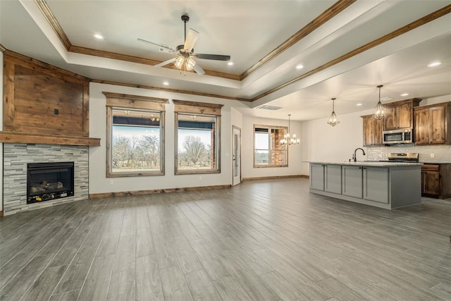 unfurnished living room with a raised ceiling, a tiled fireplace, sink, and ceiling fan with notable chandelier