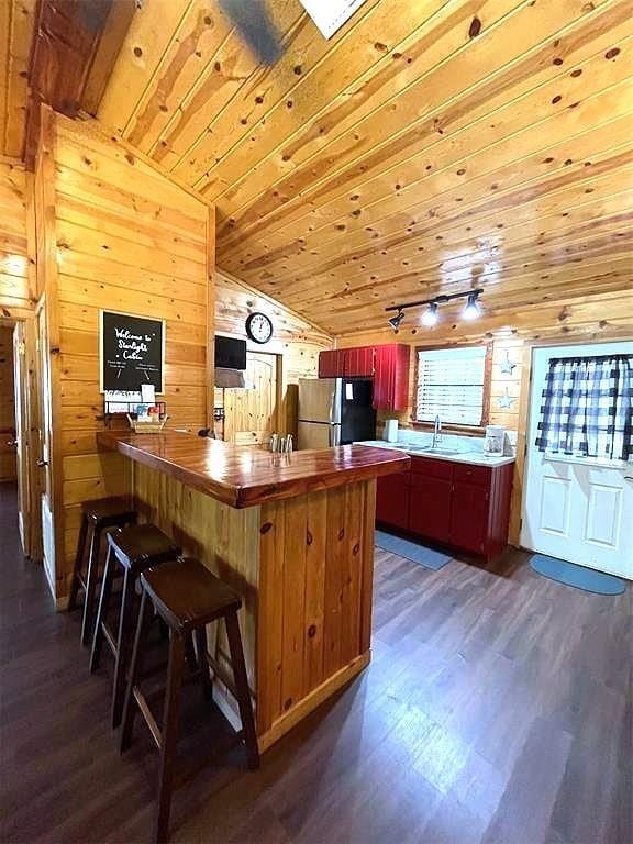 kitchen with dark wood-type flooring, wooden ceiling, stainless steel refrigerator, lofted ceiling, and wood walls