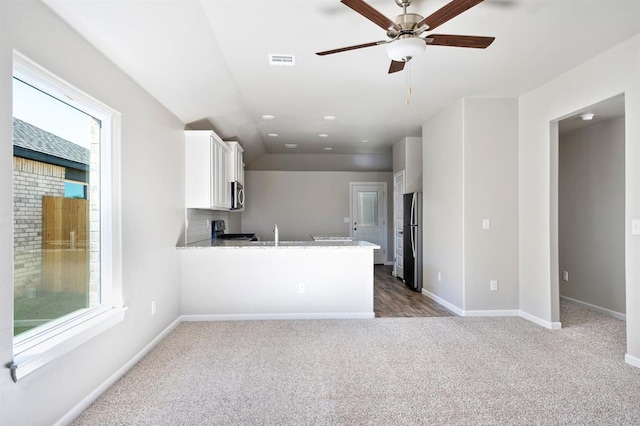 kitchen featuring kitchen peninsula, a wealth of natural light, appliances with stainless steel finishes, light colored carpet, and white cabinetry