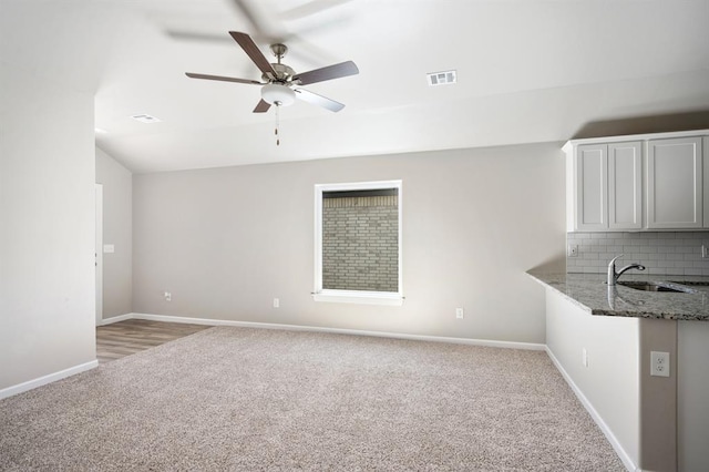 unfurnished living room with light carpet, sink, and ceiling fan