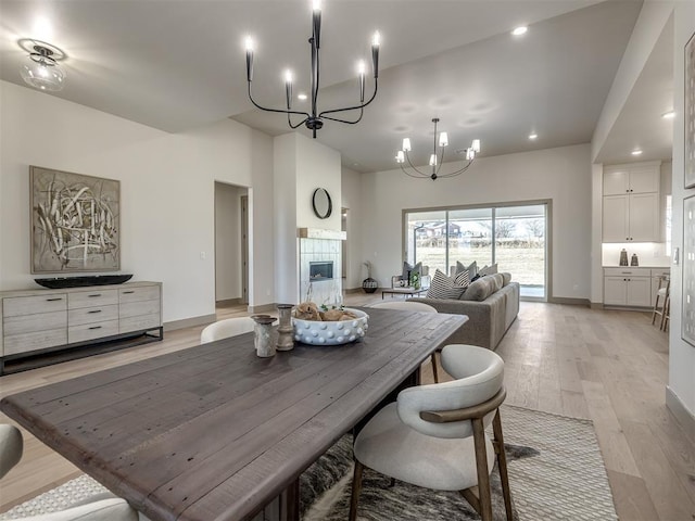 dining area with a tiled fireplace, a notable chandelier, and light hardwood / wood-style flooring