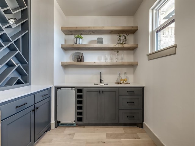 bar featuring refrigerator, sink, gray cabinetry, and light hardwood / wood-style floors