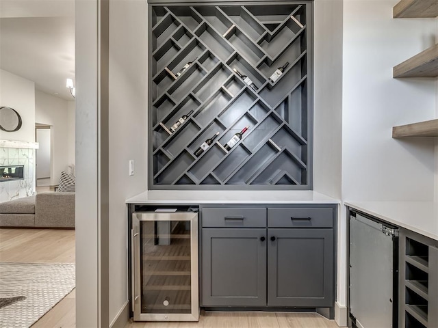 wine room with a fireplace, light wood-type flooring, bar, and wine cooler