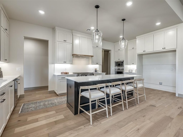 kitchen featuring white cabinets, a kitchen island, stainless steel appliances, hanging light fixtures, and light wood-type flooring