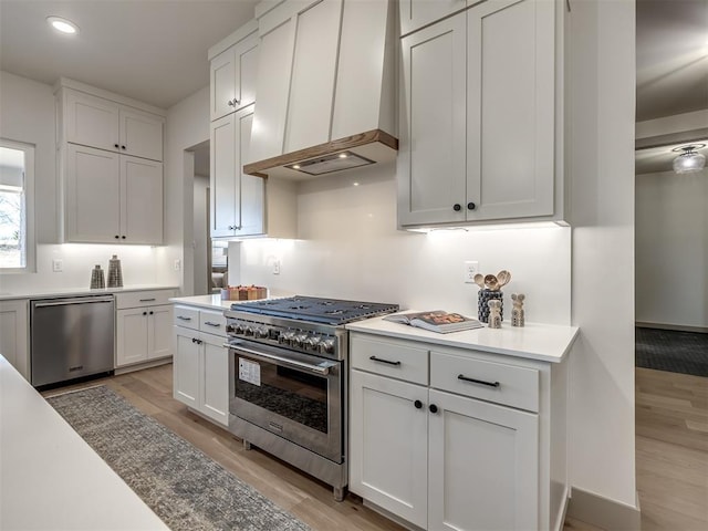 kitchen featuring premium range hood, appliances with stainless steel finishes, light hardwood / wood-style flooring, and white cabinetry