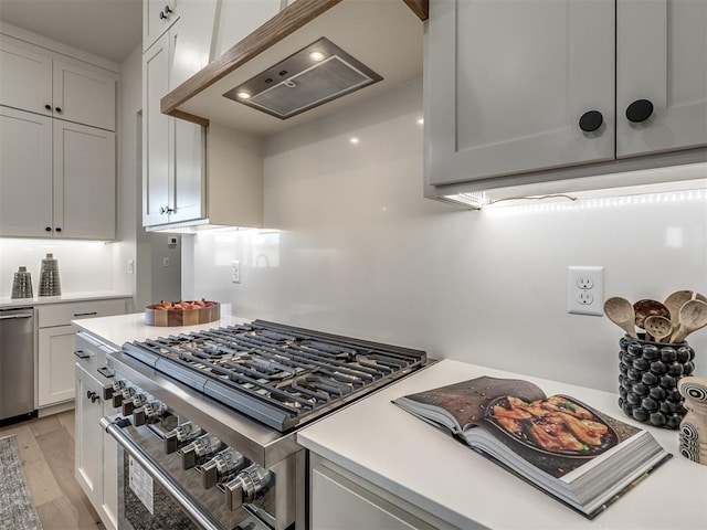 kitchen featuring light wood-type flooring, appliances with stainless steel finishes, premium range hood, and white cabinetry