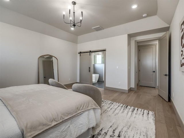 bedroom with ensuite bathroom, light hardwood / wood-style flooring, a barn door, and an inviting chandelier