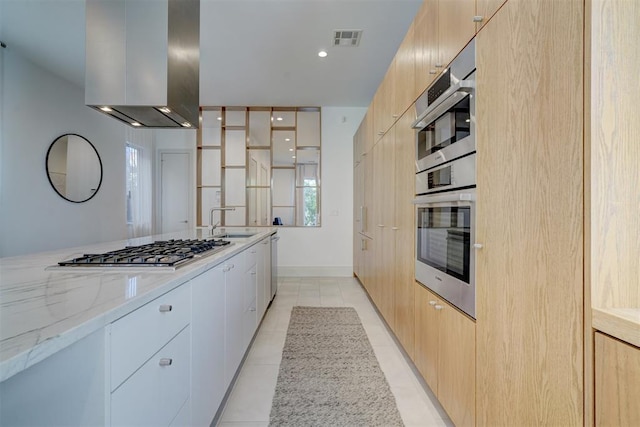 kitchen featuring light stone countertops, stainless steel gas cooktop, sink, wall chimney range hood, and white cabinets