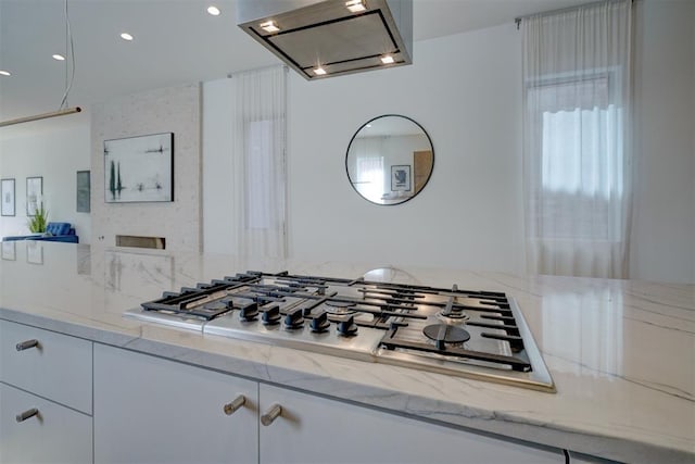 kitchen featuring white cabinetry, light stone counters, range hood, and stainless steel gas cooktop