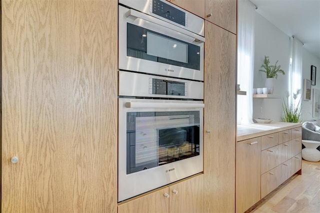 kitchen with double oven, light brown cabinetry, and light wood-type flooring