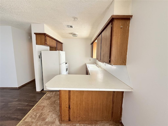 kitchen with sink, dark wood-type flooring, kitchen peninsula, white fridge, and a textured ceiling