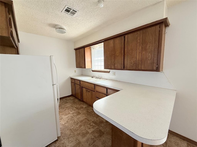 kitchen with a textured ceiling, white fridge, kitchen peninsula, and sink