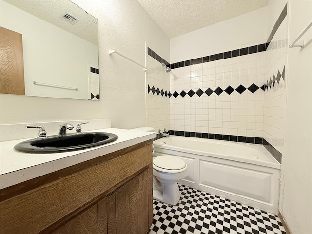 full bathroom with tiled shower / bath combo, toilet, a textured ceiling, and vanity