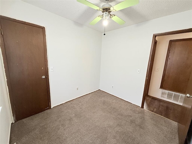 unfurnished bedroom with ceiling fan, dark carpet, and a textured ceiling