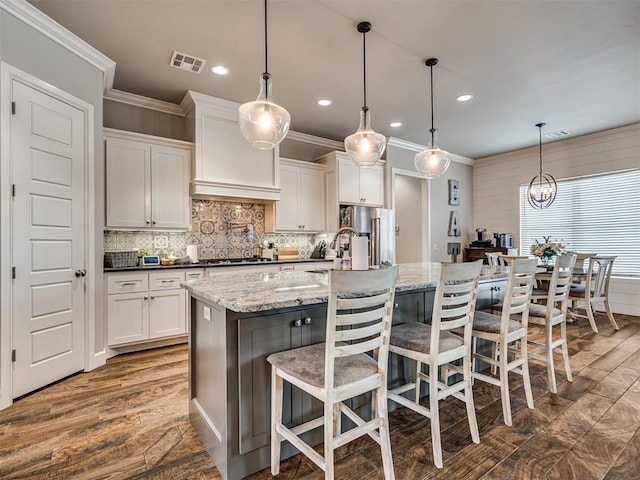 kitchen featuring pendant lighting, dark stone countertops, a breakfast bar area, white cabinets, and a kitchen island with sink