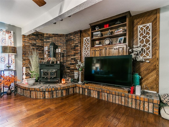 living room with hardwood / wood-style flooring, ceiling fan, a wood stove, and wooden walls