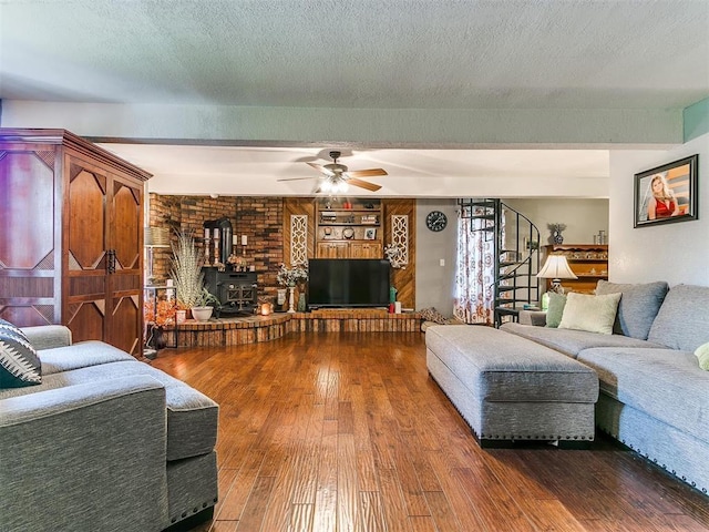 living room featuring a wood stove, ceiling fan, hardwood / wood-style floors, and a textured ceiling