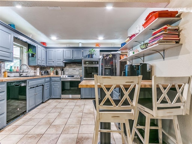 kitchen with wood counters, decorative backsplash, sink, black appliances, and light tile patterned flooring