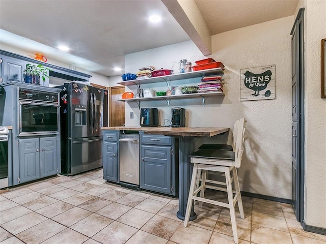 kitchen with blue cabinetry, a kitchen breakfast bar, wooden counters, light tile patterned floors, and black appliances