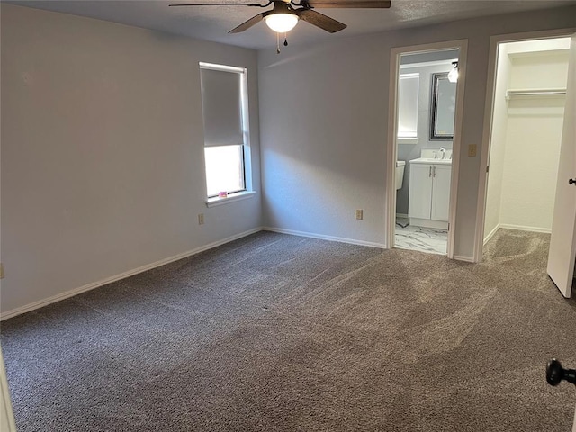 unfurnished bedroom featuring ensuite bath, ceiling fan, a walk in closet, a closet, and carpet