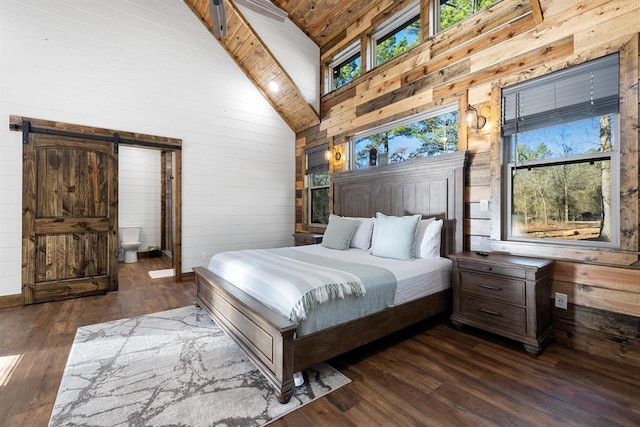 bedroom with a barn door, dark wood-type flooring, high vaulted ceiling, and multiple windows