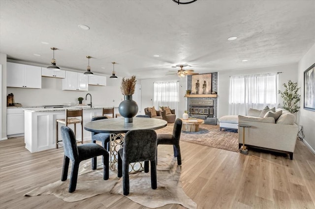 dining space featuring a wealth of natural light, ceiling fan, a fireplace, and light wood-type flooring