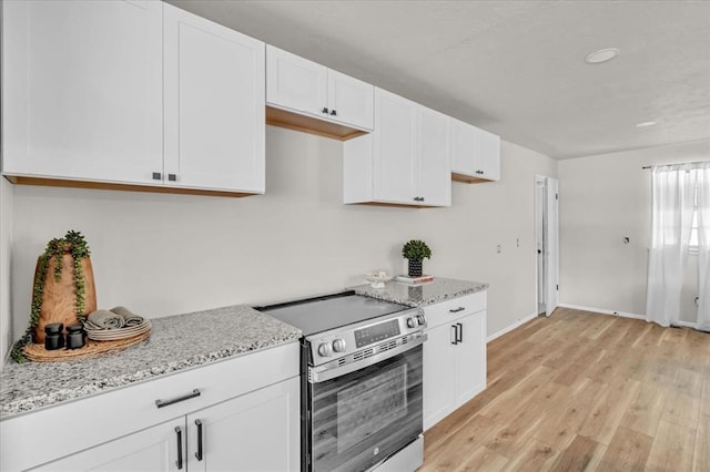 kitchen with electric stove, light stone countertops, white cabinets, and light wood-type flooring