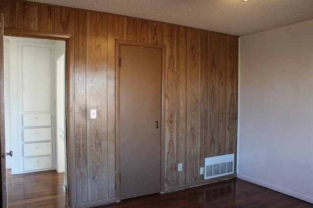 unfurnished bedroom with a textured ceiling, wooden walls, and dark wood-type flooring