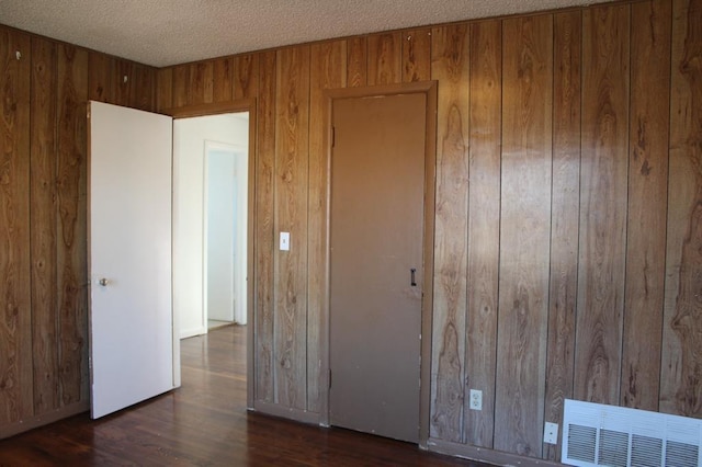 unfurnished bedroom featuring dark hardwood / wood-style flooring, a textured ceiling, and wooden walls