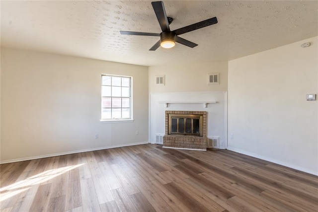 unfurnished living room with a textured ceiling, ceiling fan, wood-type flooring, and a fireplace