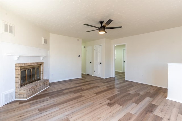 unfurnished living room with ceiling fan, light hardwood / wood-style flooring, a textured ceiling, and a brick fireplace