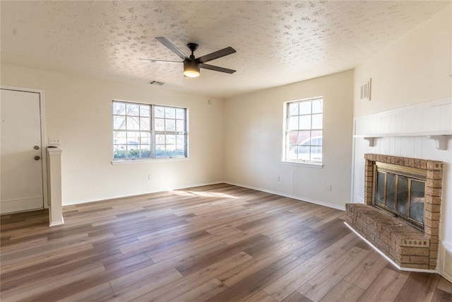 unfurnished living room with hardwood / wood-style floors, a healthy amount of sunlight, a textured ceiling, and a brick fireplace