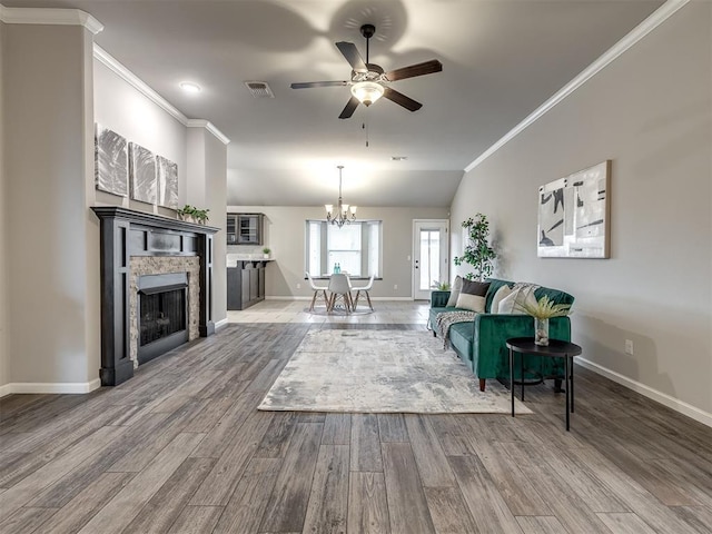 living room featuring crown molding, visible vents, a stone fireplace, wood finished floors, and ceiling fan with notable chandelier