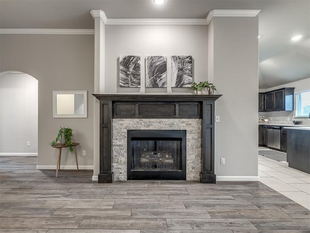 interior details with arched walkways, a stone fireplace, stainless steel dishwasher, ornamental molding, and wood tiled floor