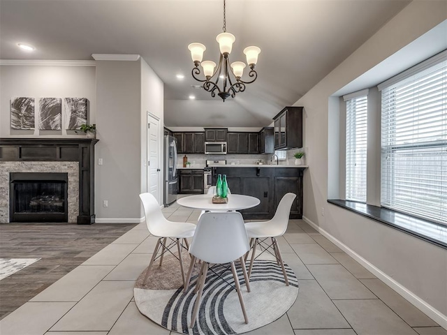 dining area featuring light tile patterned floors, a chandelier, a fireplace, baseboards, and crown molding