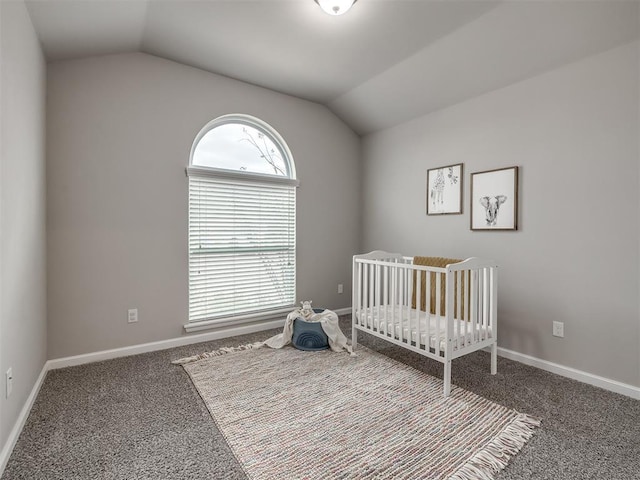 bedroom with vaulted ceiling, a crib, carpet flooring, and baseboards