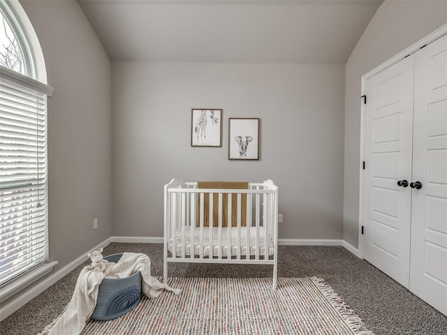 unfurnished bedroom with carpet floors, a closet, a crib, and baseboards