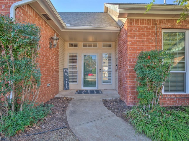 entrance to property featuring brick siding and a shingled roof