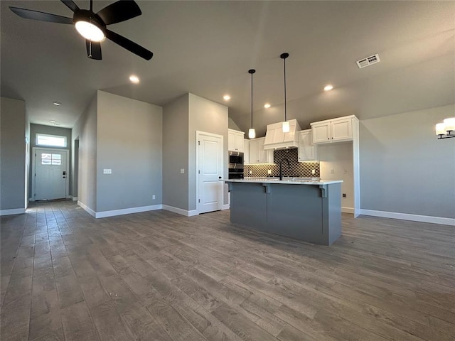 kitchen with a center island with sink, light countertops, visible vents, open floor plan, and white cabinetry