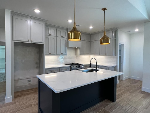 kitchen featuring light stone countertops, sink, decorative light fixtures, a kitchen island with sink, and high end stainless steel range