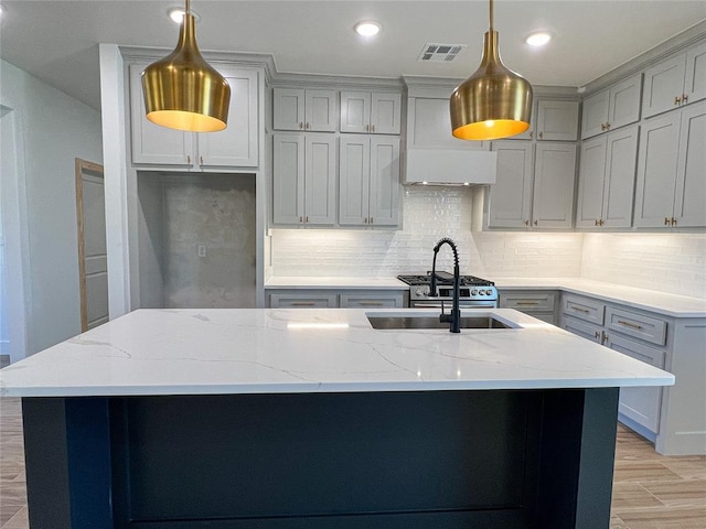 kitchen featuring light stone countertops, decorative light fixtures, tasteful backsplash, and a kitchen island with sink