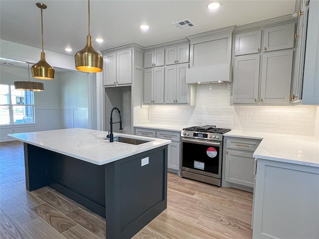 kitchen featuring gray cabinetry, sink, stainless steel gas range, light stone counters, and decorative light fixtures