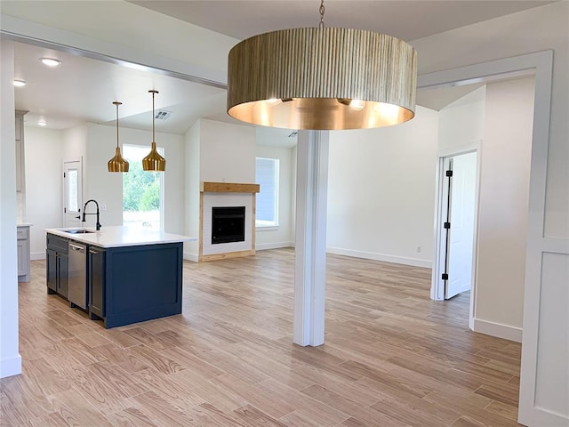 kitchen featuring sink, light hardwood / wood-style flooring, stainless steel dishwasher, an island with sink, and decorative light fixtures